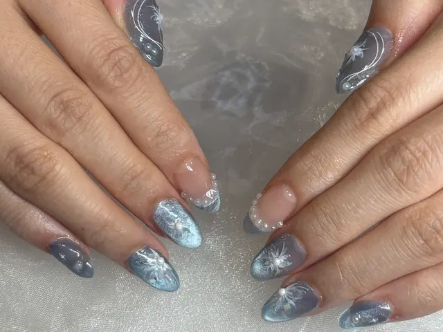 Medium almond Gel-X nails in icy steel-blue cat-eye polish with silver celestial details and pearls